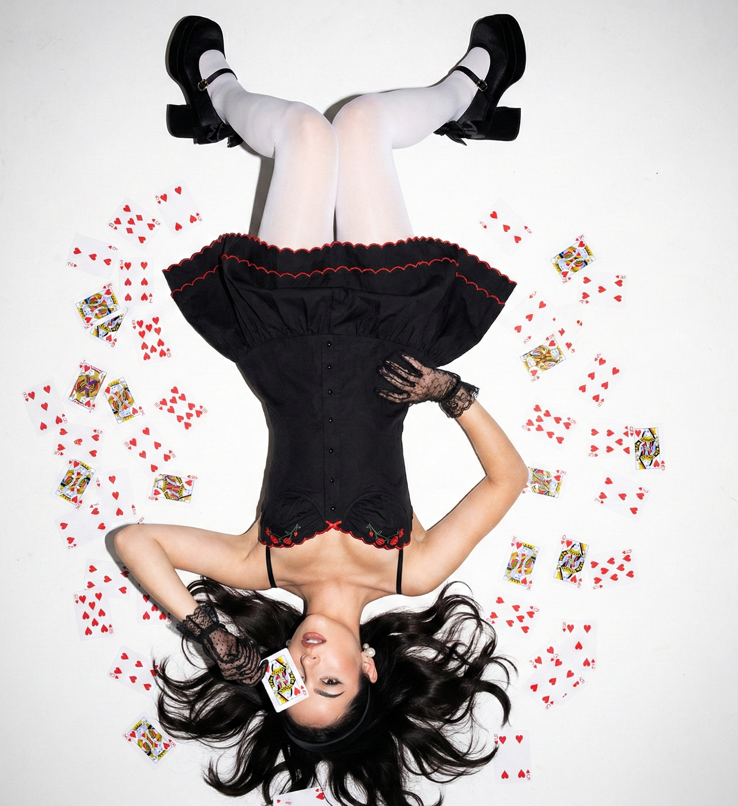Woman in a black dress surrounded by playing cards on a white background